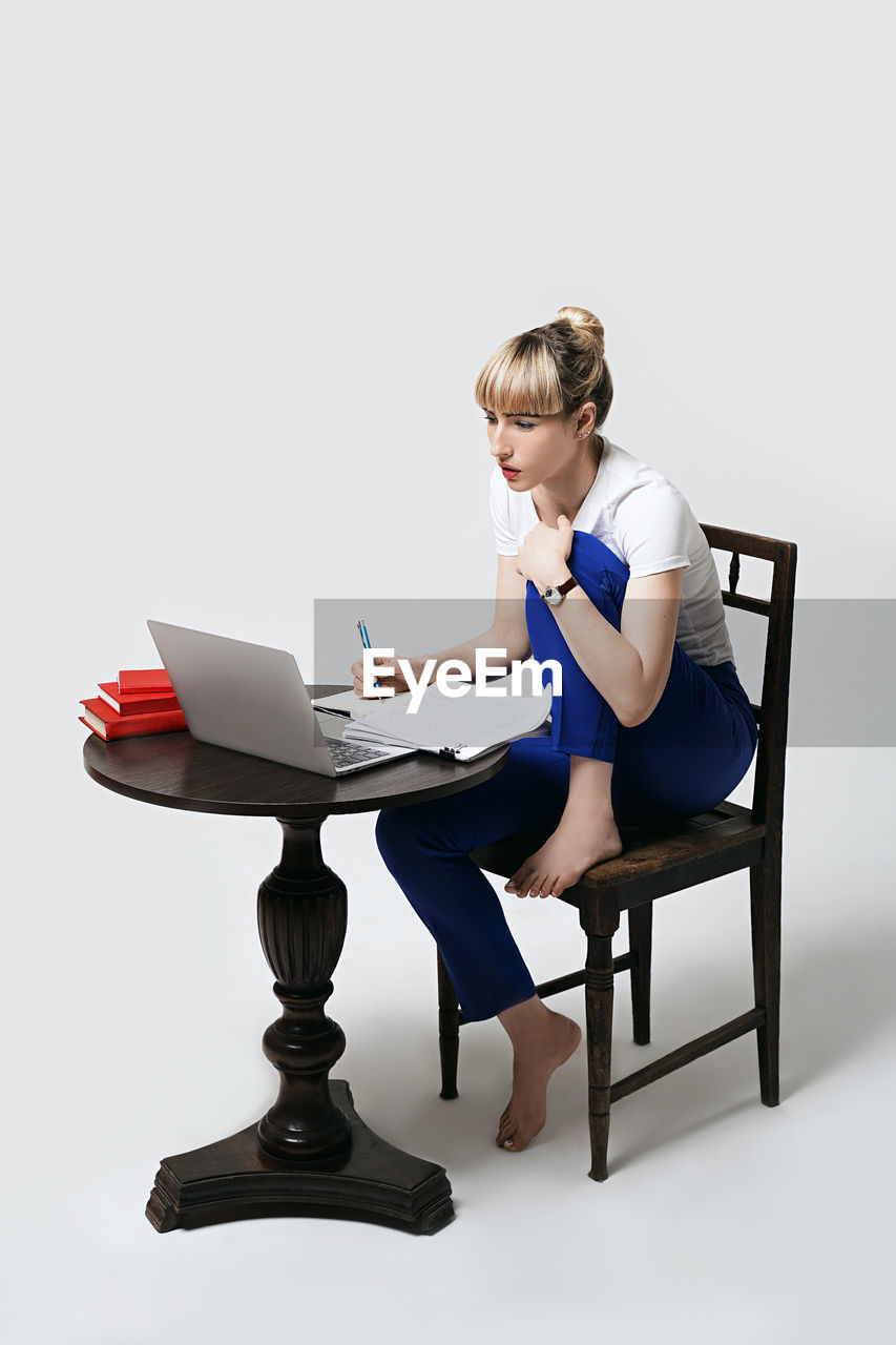 side view of young woman using laptop while sitting on chair against white background