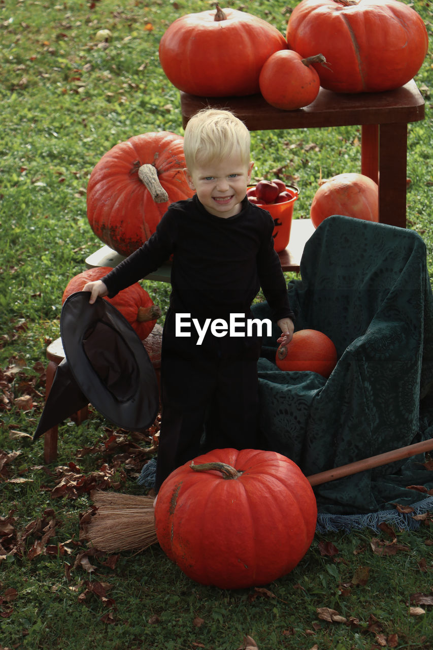 Full length of boy holding pumpkin on field. child in halloween costume 