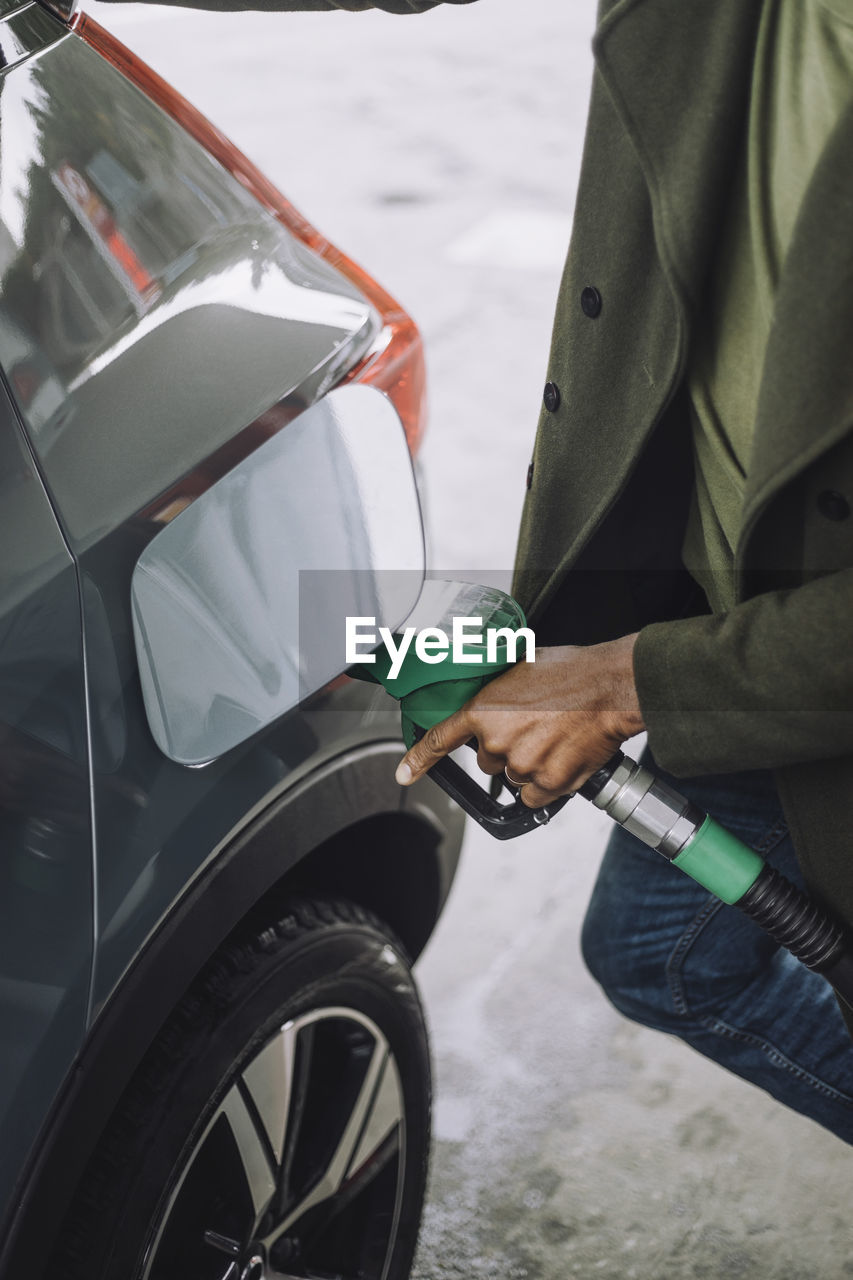 Midsection of man refueling car at fuel station