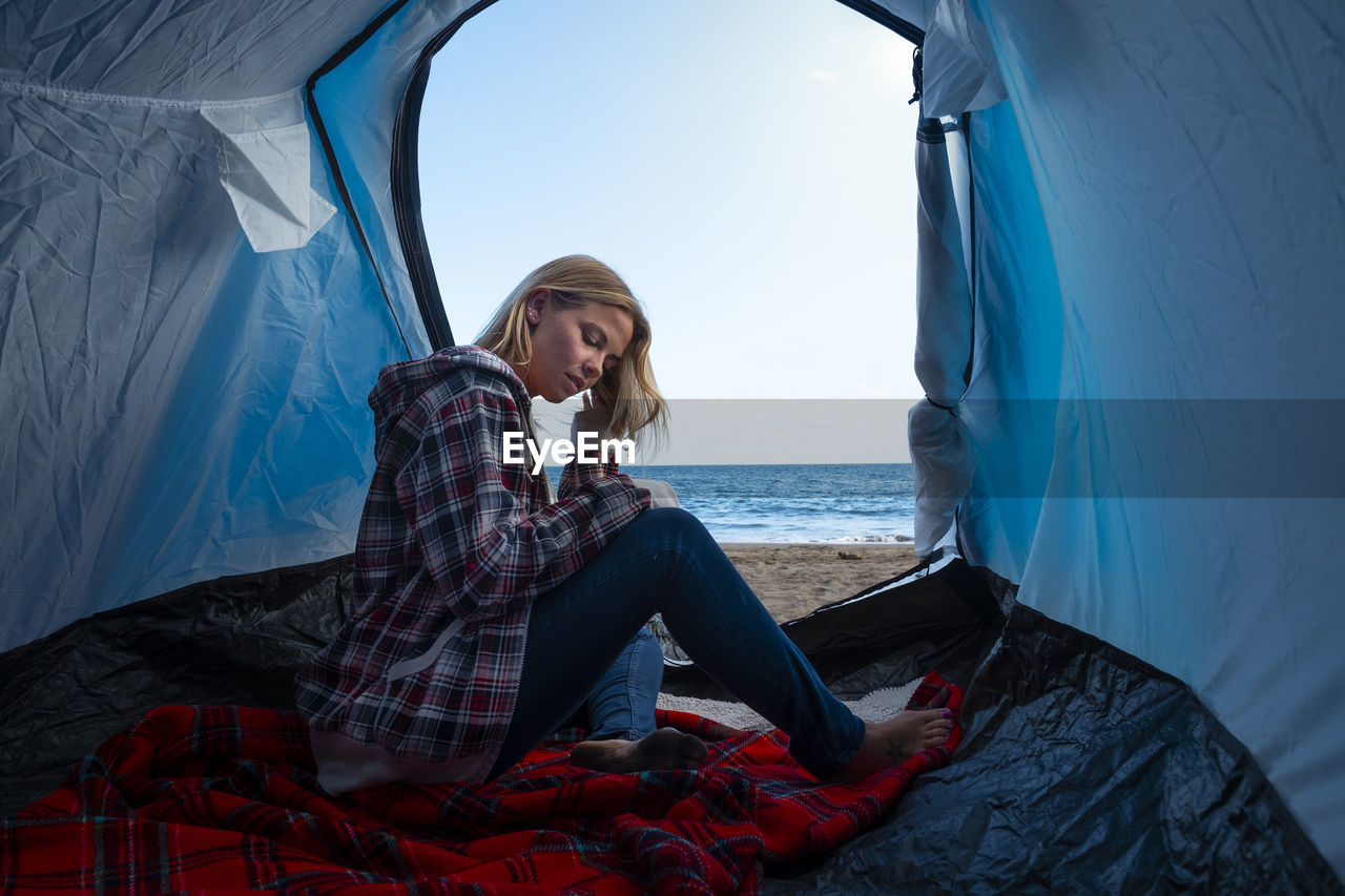 Woman sitting in tent at beach against sea and sky