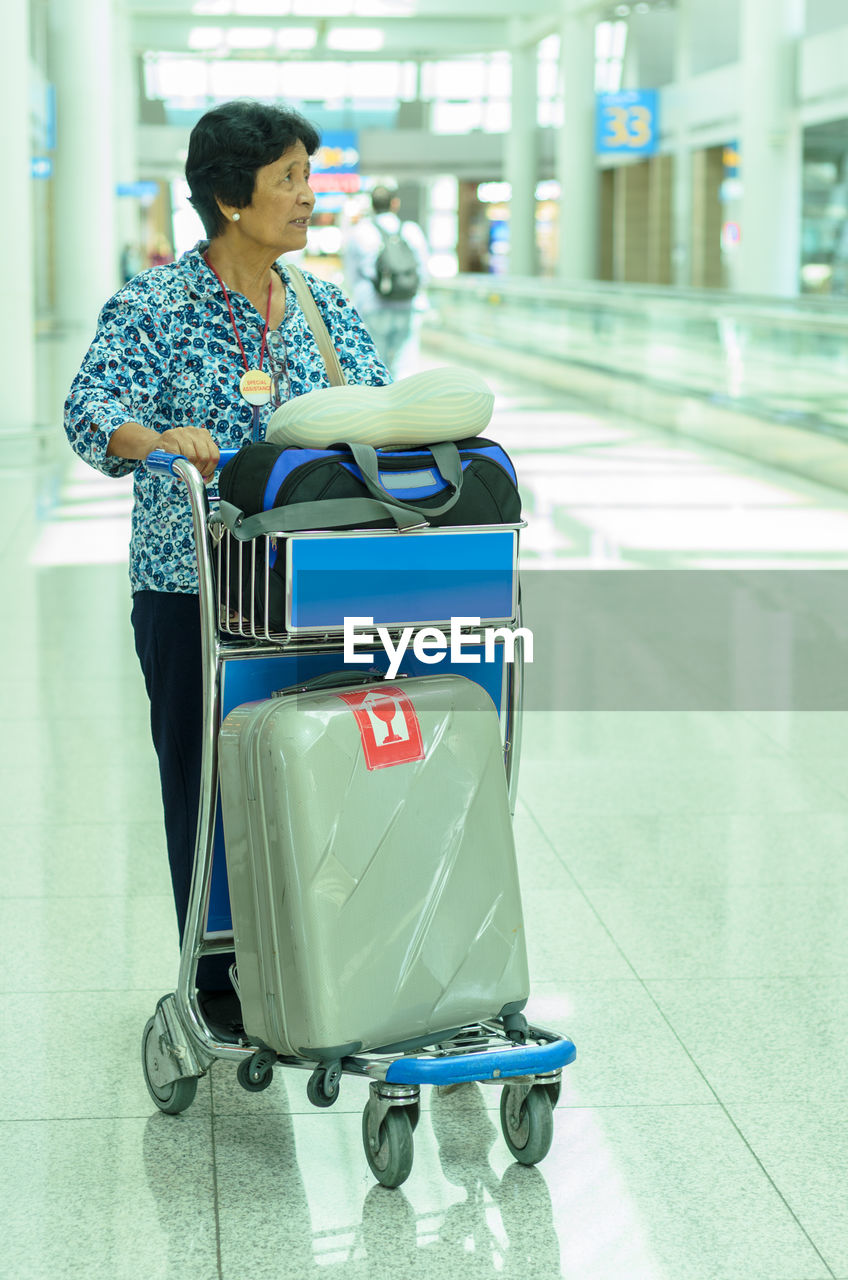 Senior woman with luggage in cart standing at airport