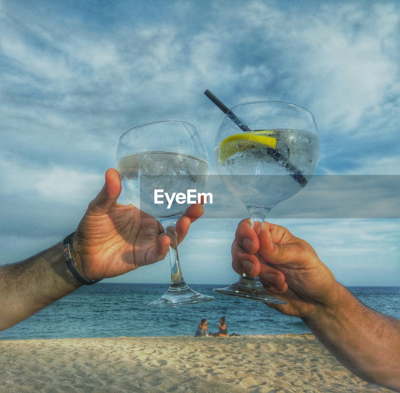 Cropped image of friends toasting drink at beach against sky