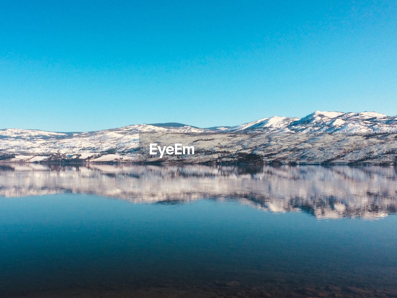 Scenic view of lake and snowcapped mountains against clear blue sky