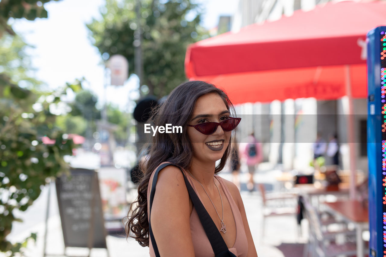 Smiling young woman looking away while wearing sunglasses in city
