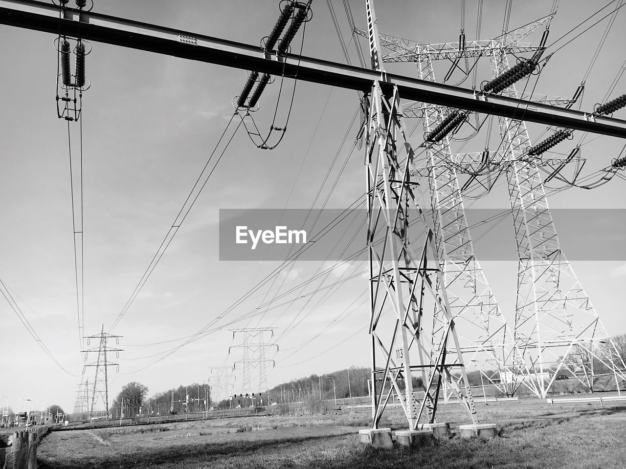 Low angle view of electricity pylons on field against sky