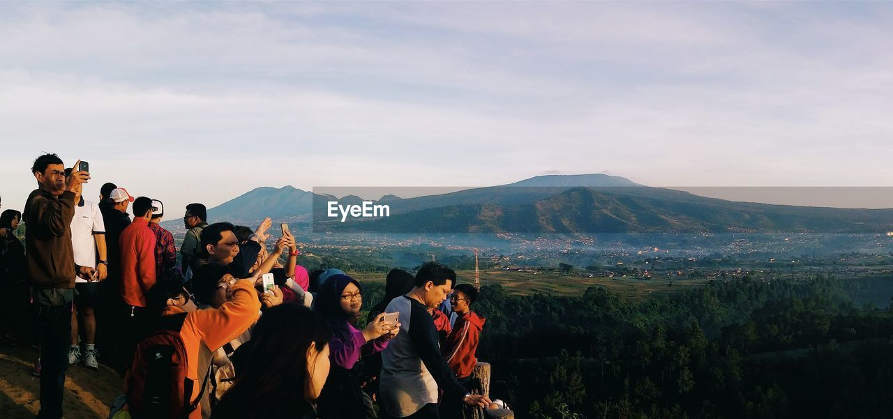 Crowd standing on field in front of mountains against cloudy sky