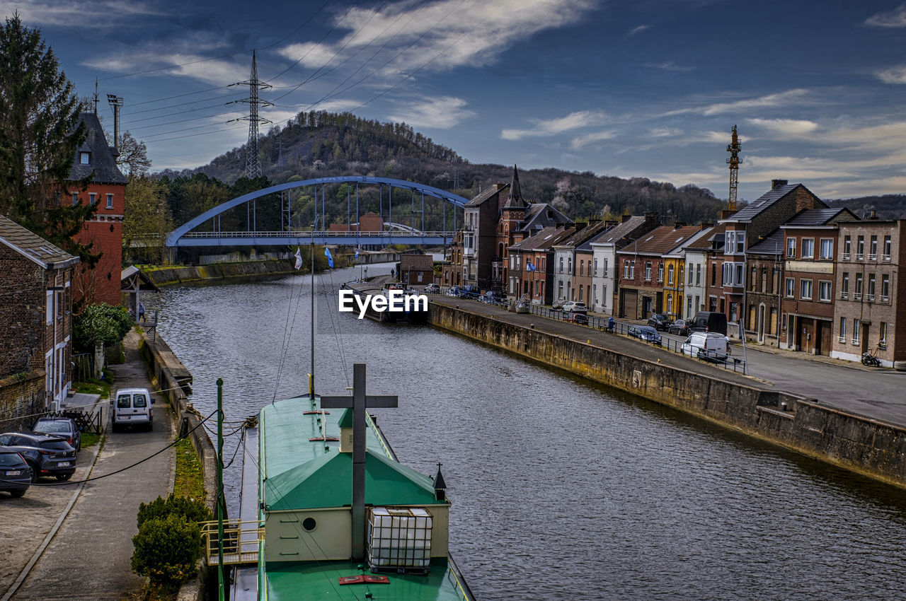 Bridge over river by buildings in city against sky