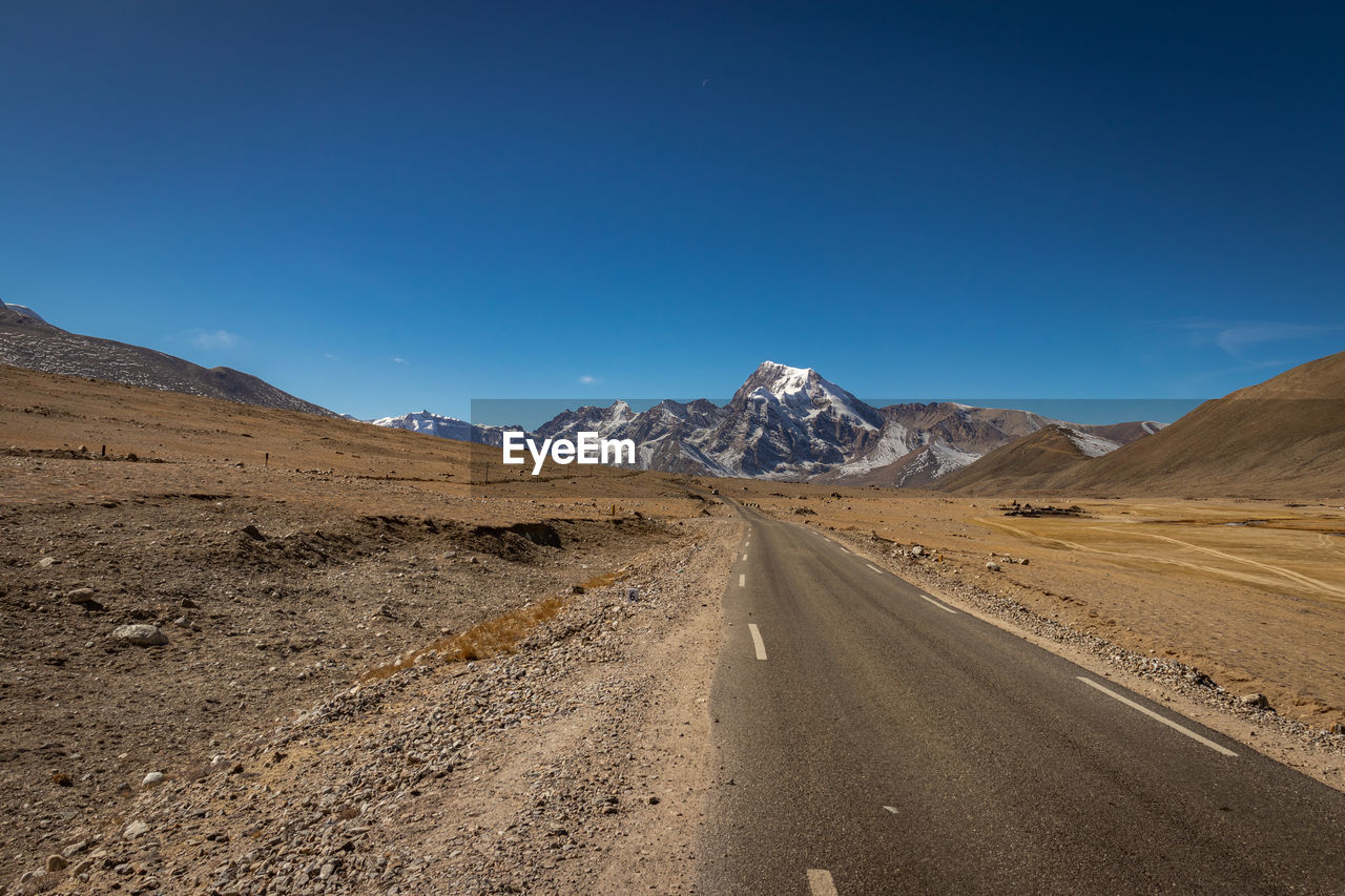 Road leading towards mountains against blue sky