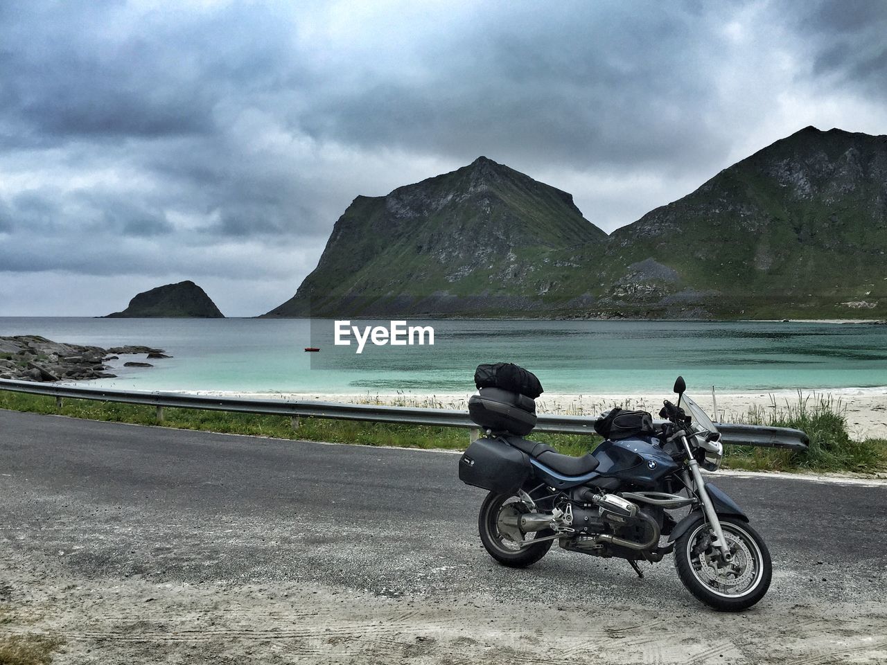Motorcycle on road by sea against cloudy sky