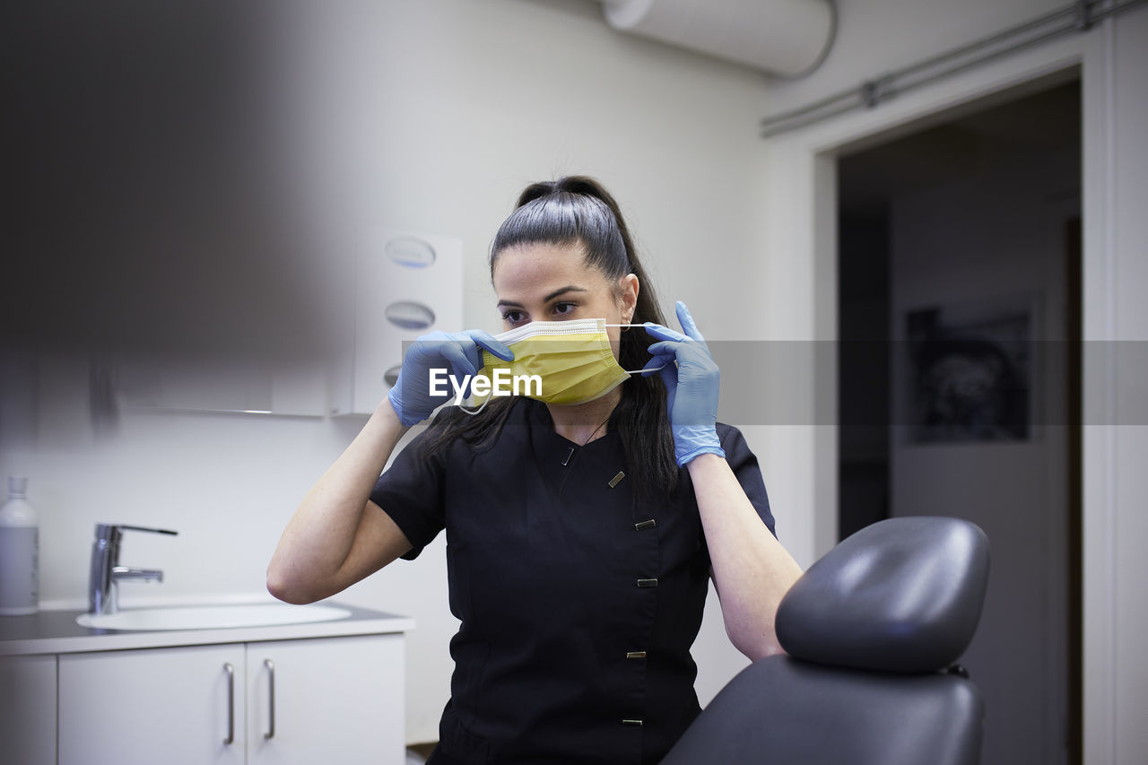 Female dentist putting protective face mask on