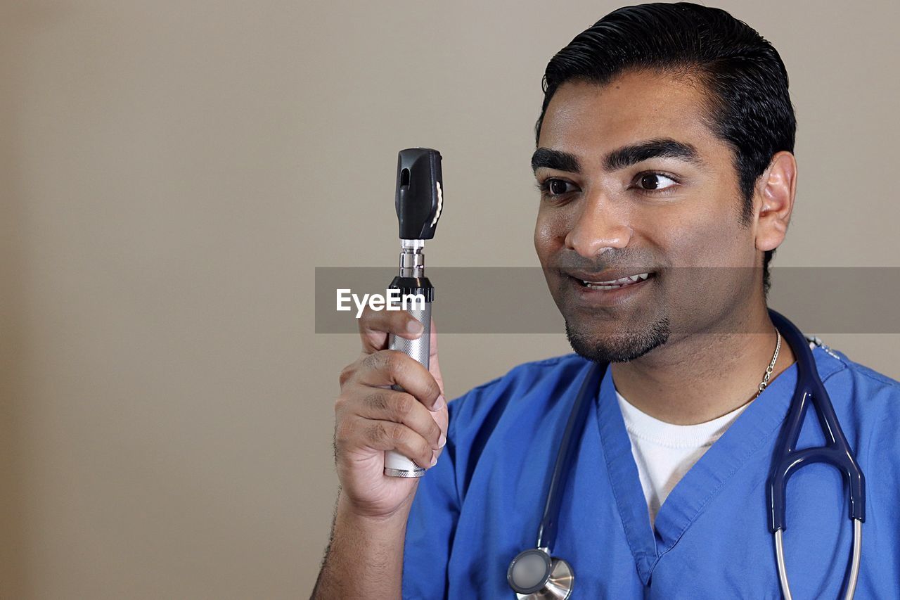 Smiling doctor looking through ophthalmoscope against beige background