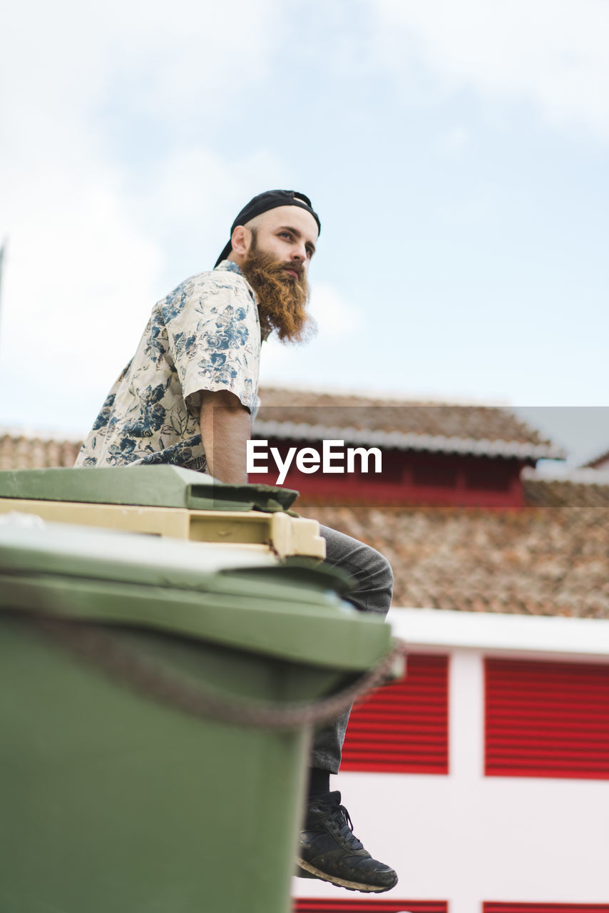 Male hipster tourist sitting on garbage bin