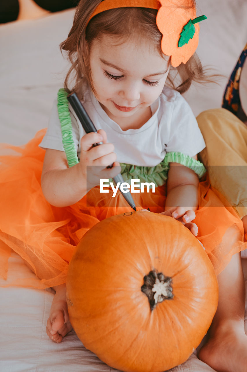 Little toddler girl drawing on a pumpkin making lantern jack on halloween holiday. 