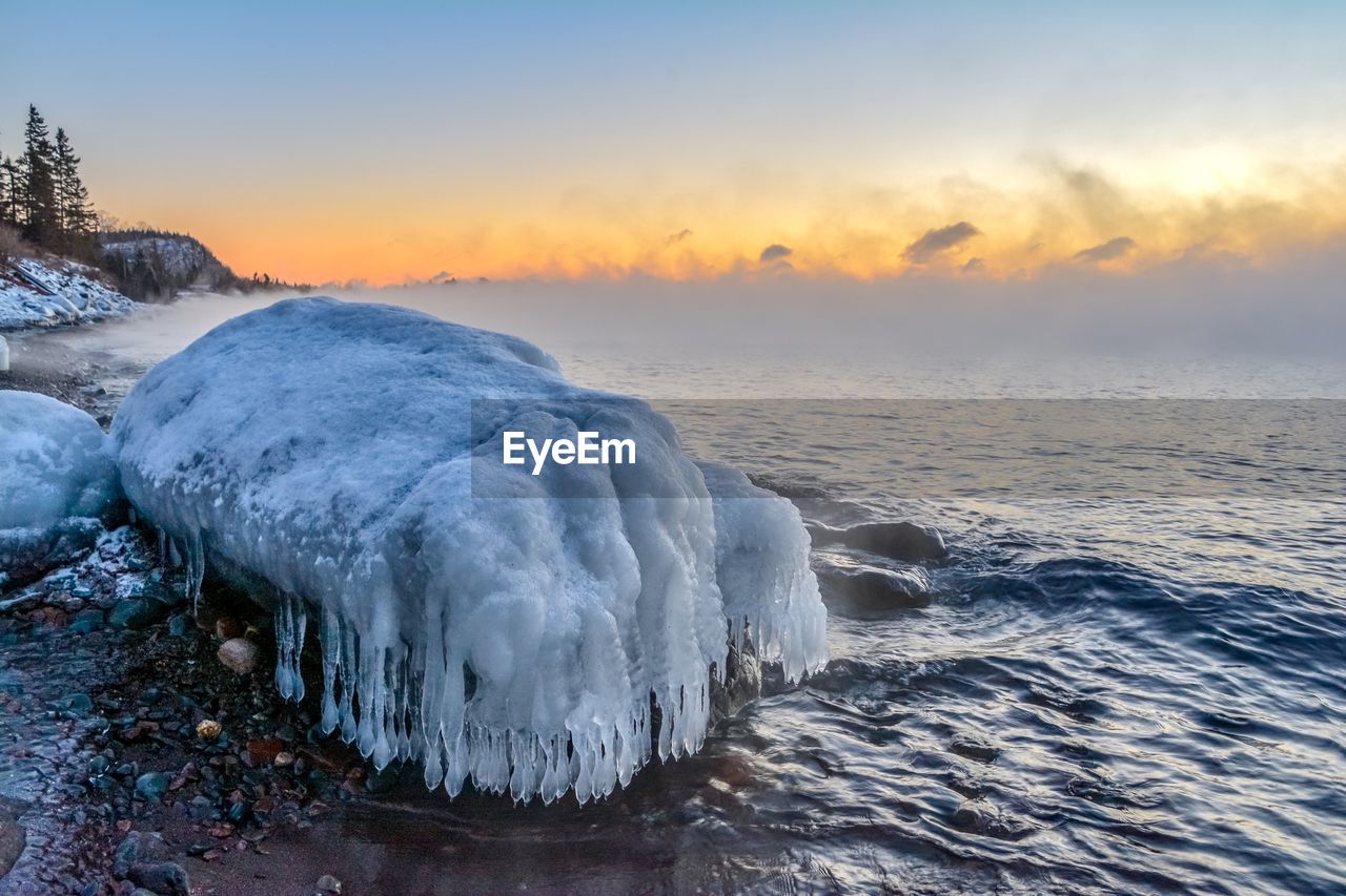 Frozen sea against sky during sunset