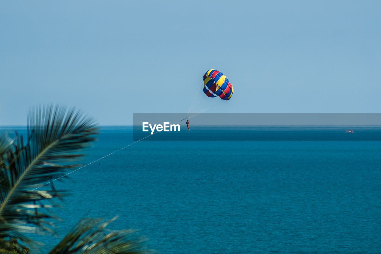 Person parasailing over sea against clear sky