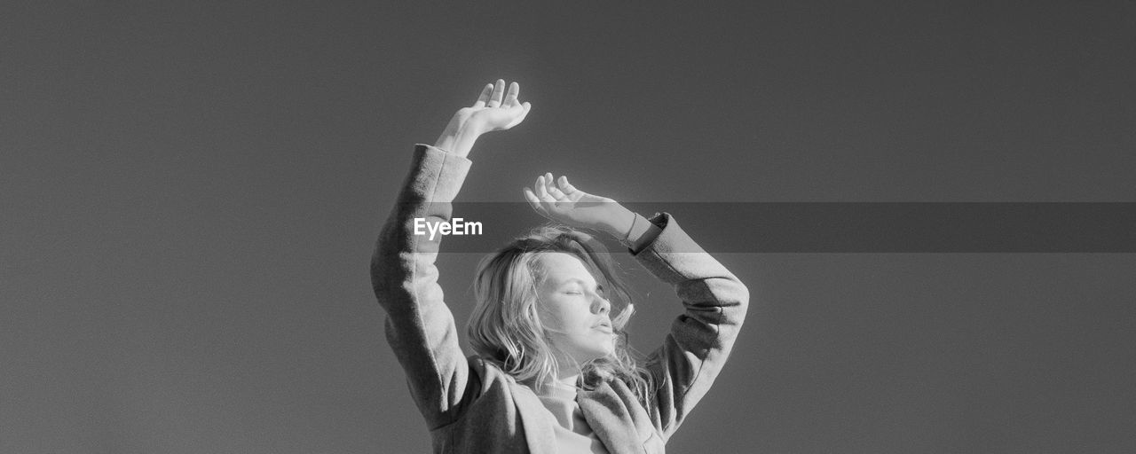 Low angle view of woman with arms raised against clear sky