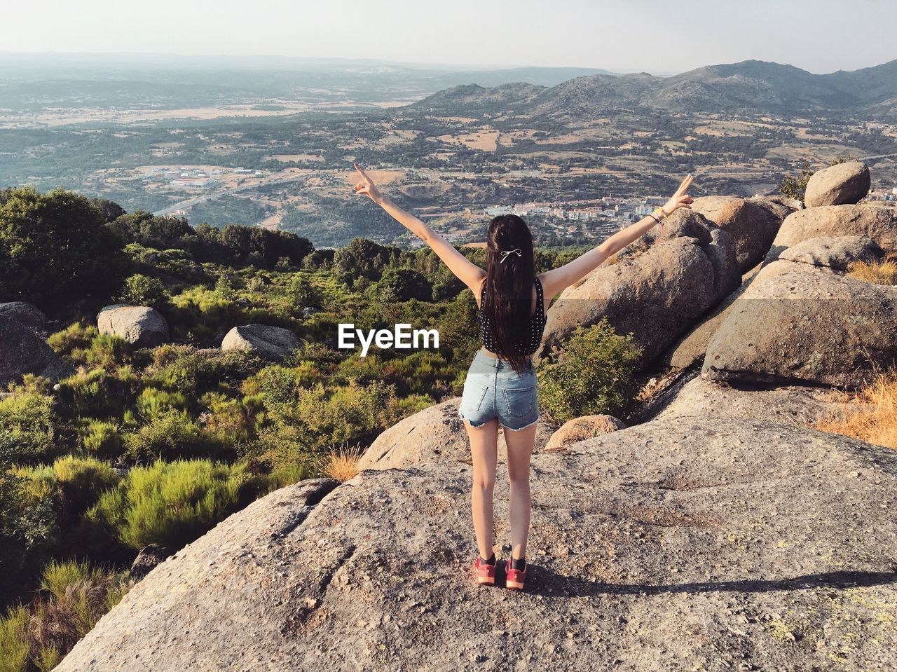 Full length rear view of woman standing on rock with arms outstretched against landscape