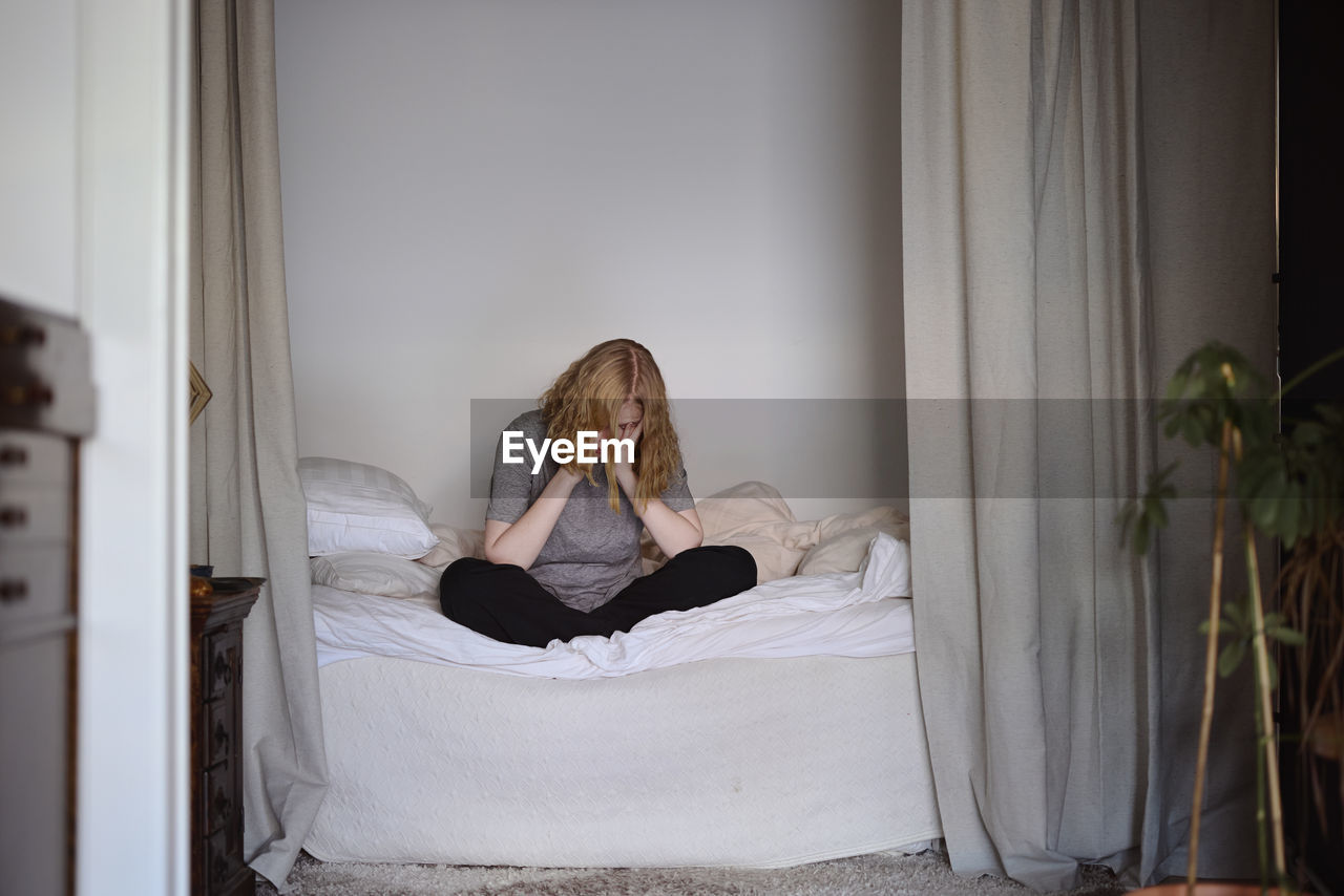 Crying young woman sitting on bed