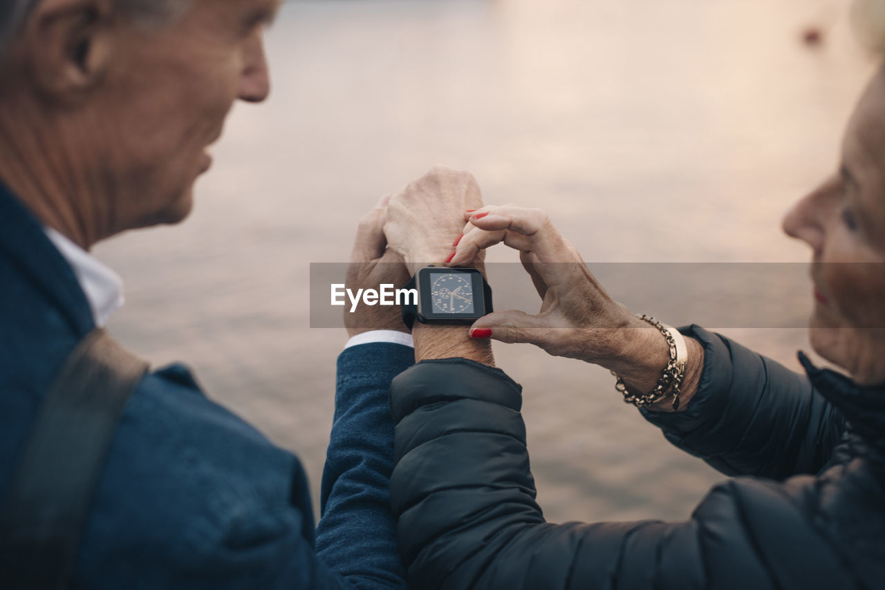 Cropped image of senior woman showing time to man on smart watch
