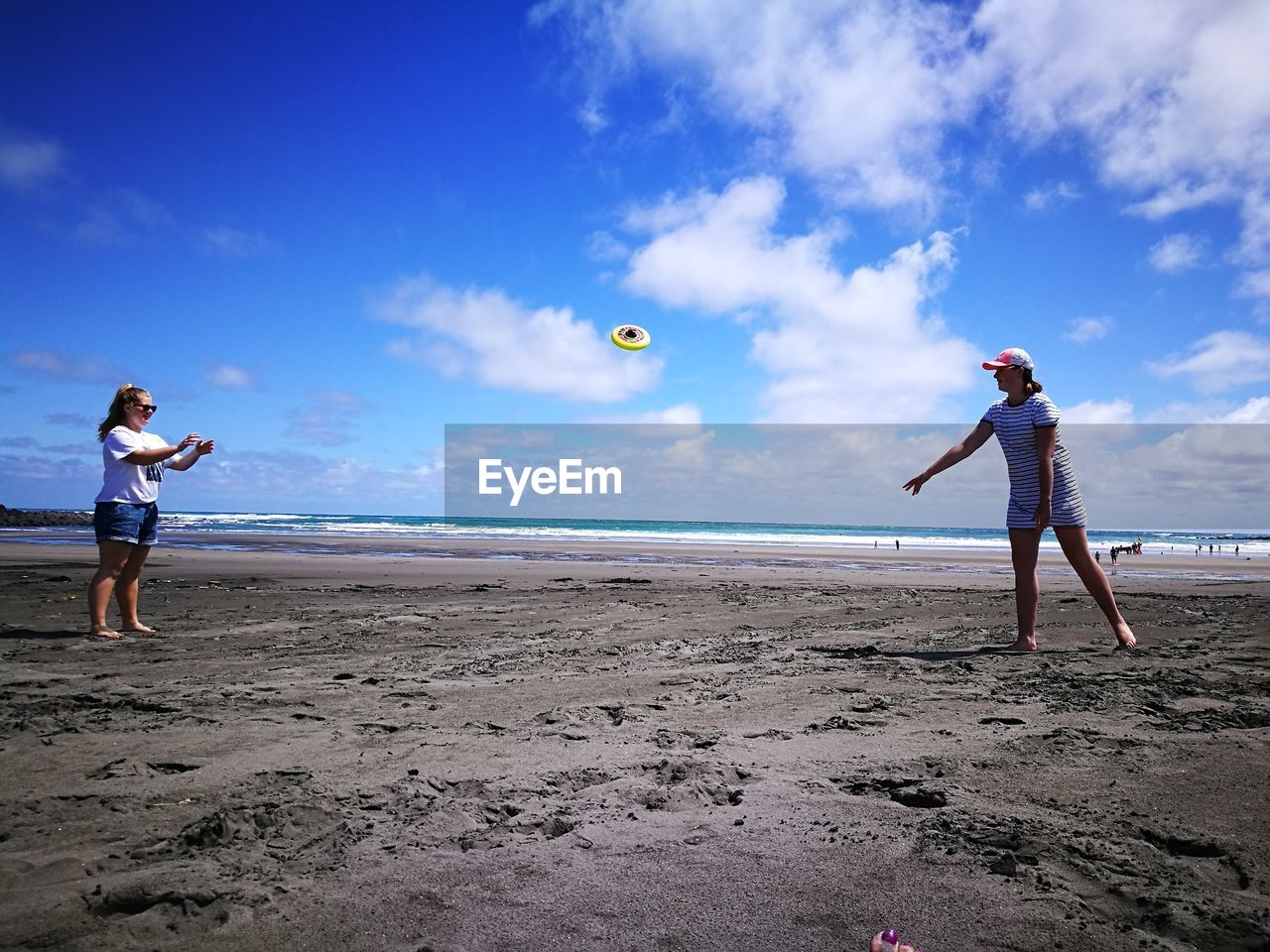 Friends playing plastic disc on shore at beach against sky