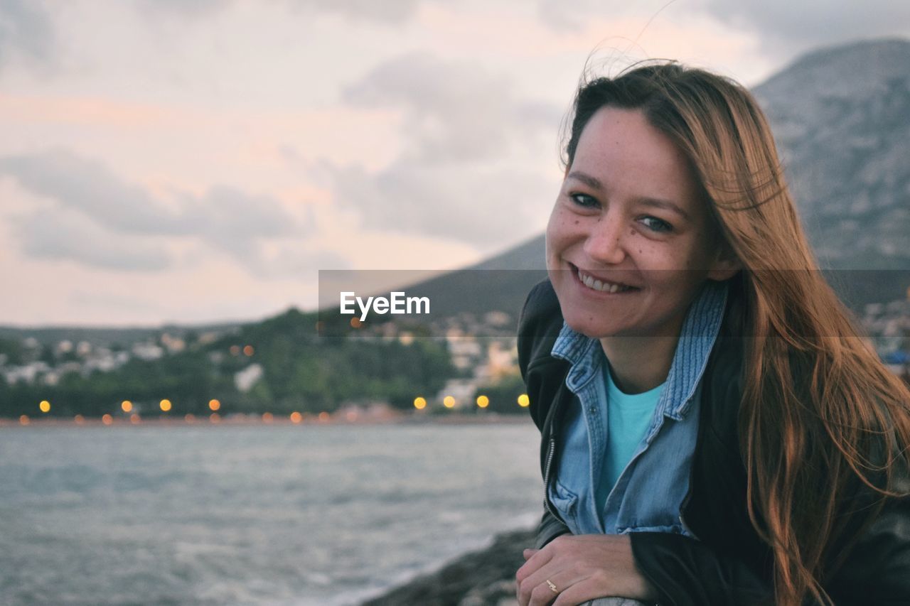 Portrait of smiling woman against river during sunset