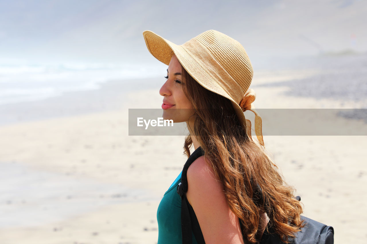 Side view of young woman with long hair standing at beach