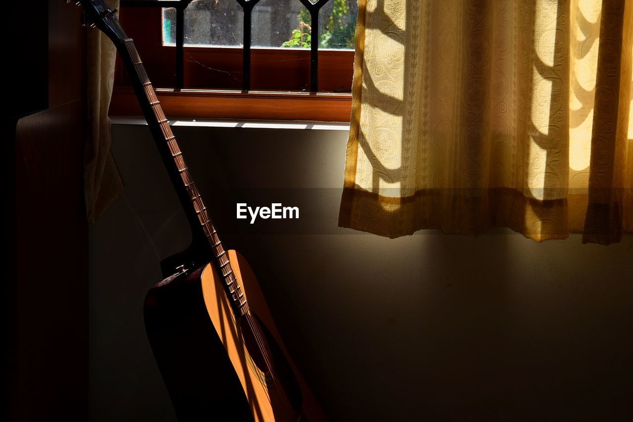 Close-up of guitar by window at home