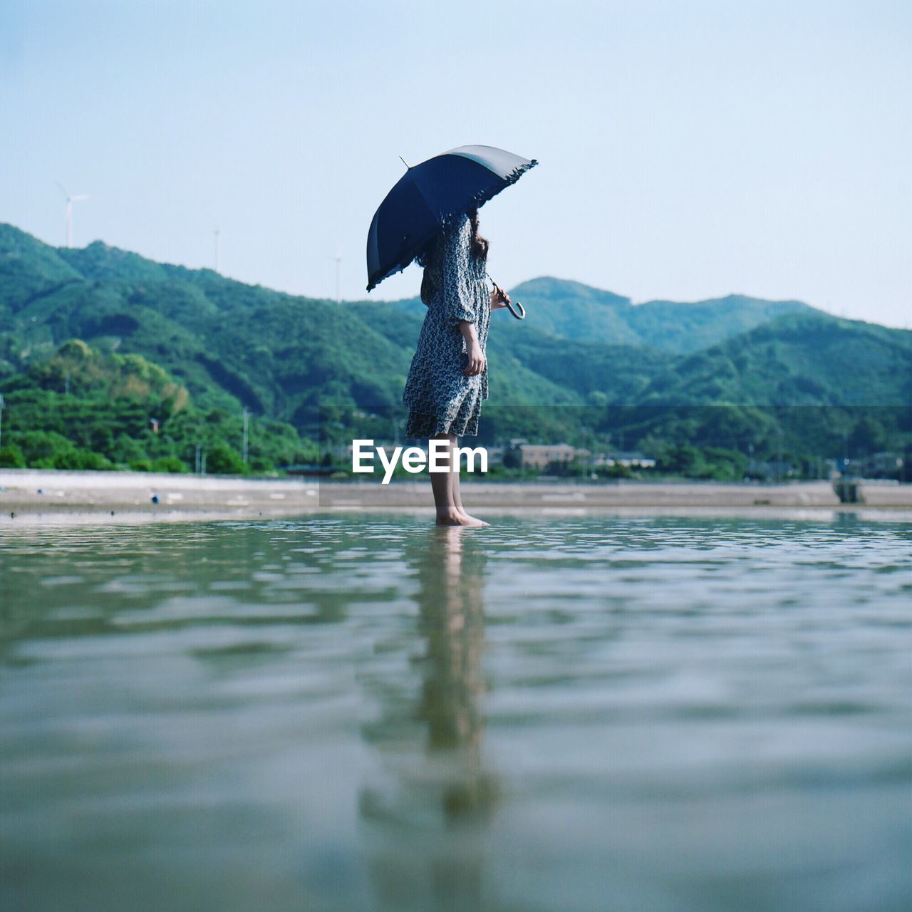 Woman holding umbrella on beach against clear sky