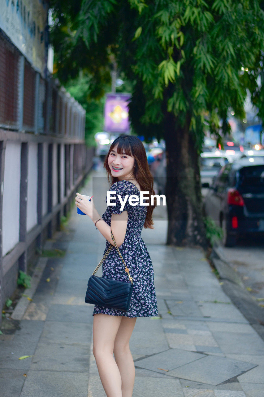 portrait of young woman standing on footpath in city