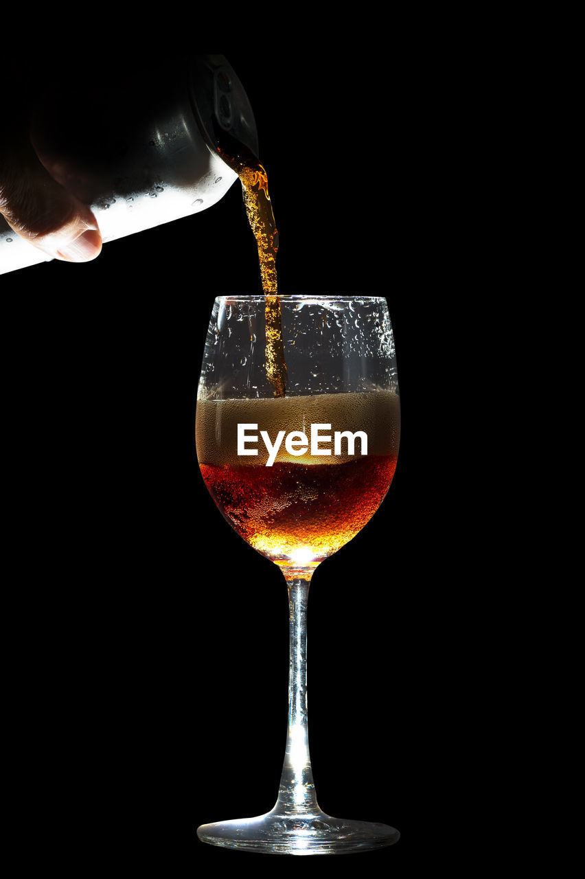 Close-up of beer being poured in wineglass against black background