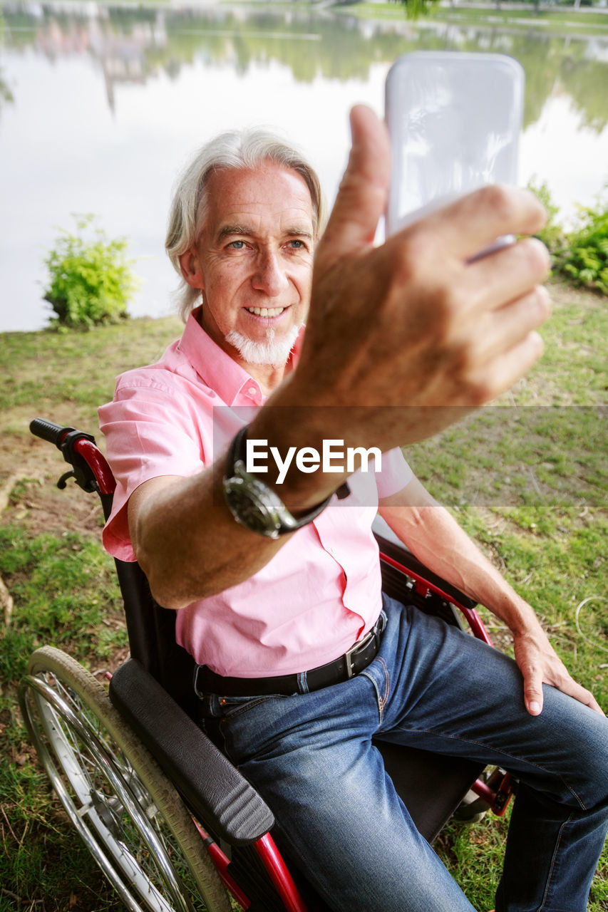 Smiling senior man photographing while sitting on wheelchair