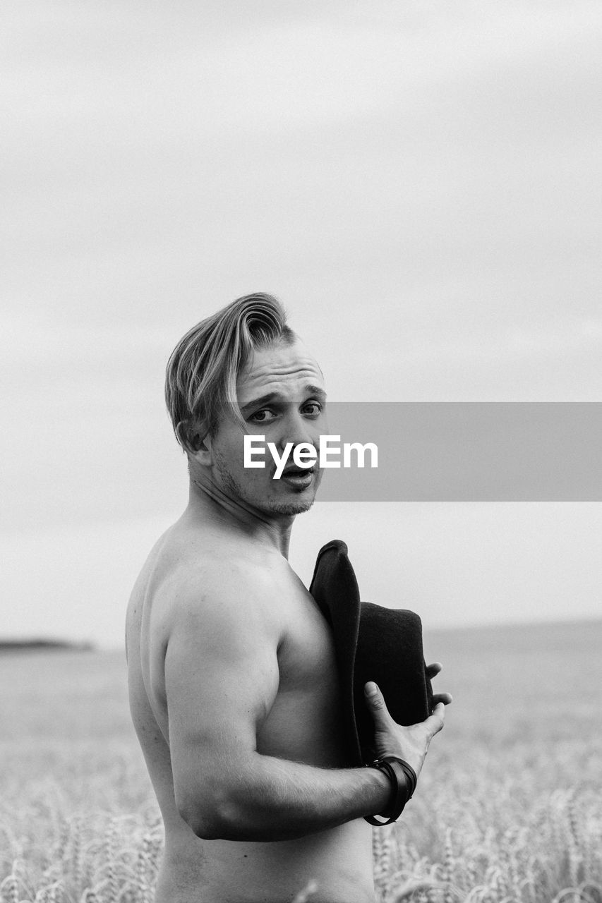 Side view of shirtless man standing at beach against sky