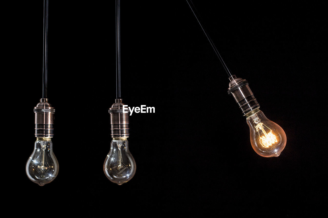 Close-up of light bulbs hanging against black background