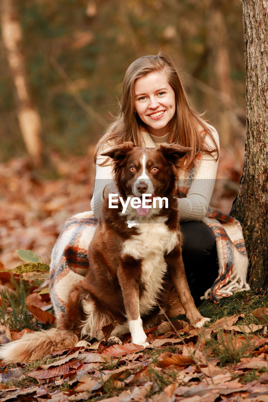 Portrait of smiling young woman with dog at forest