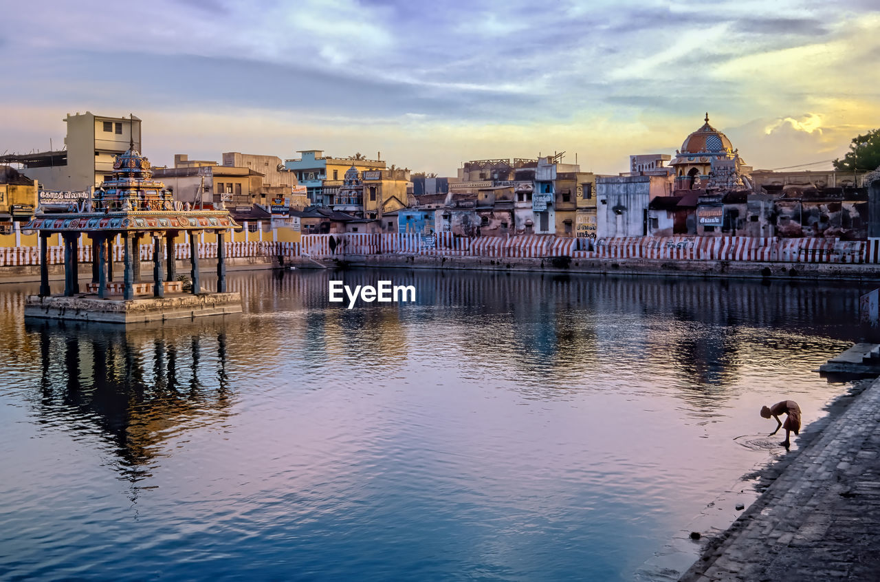 Holy tank of hindu temple with pavilion against background of houses at sunset. 