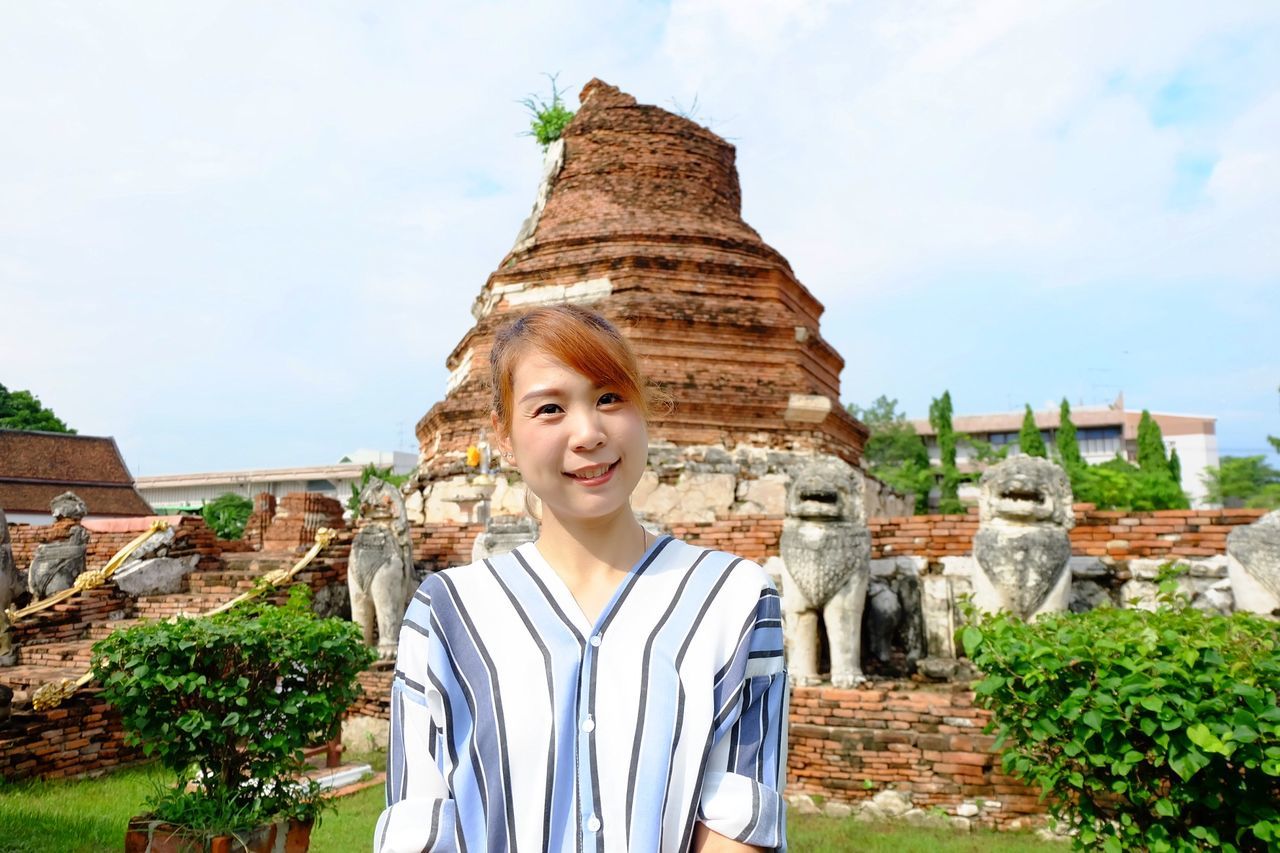 Portrait of young woman standing at wat thammikarat against sky