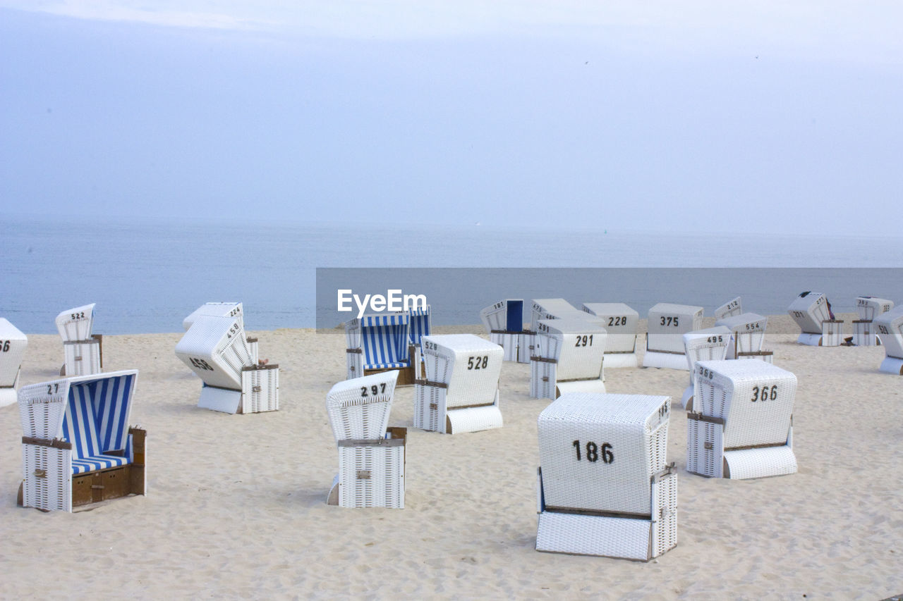 Tilt-shift image of hooded beach chairs with numbers on sand at beach against sky