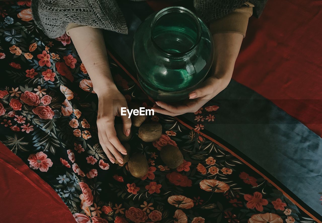 Cropped hand of woman holding container with kiwi on floor