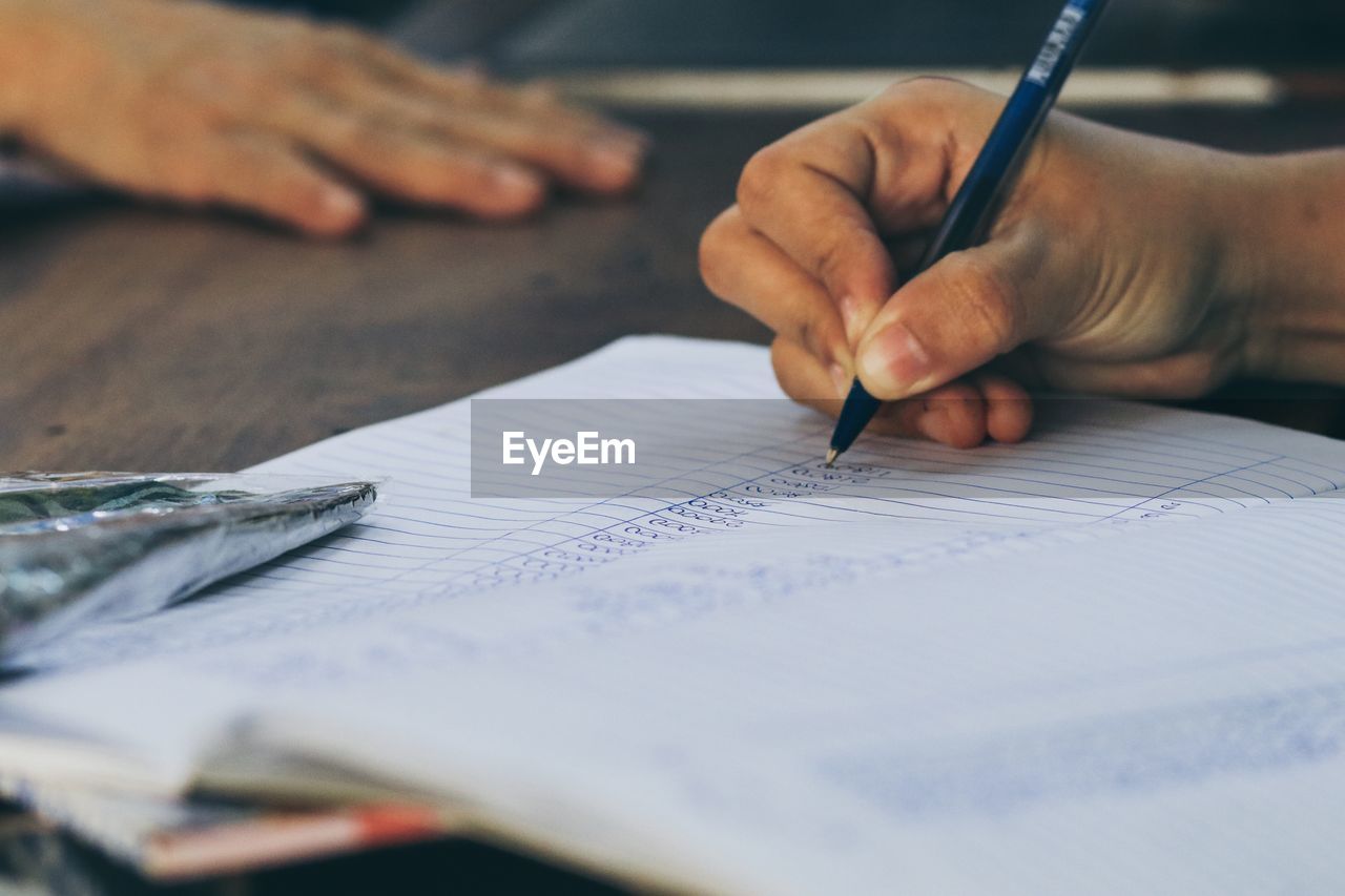 Cropped hand writing in book at table