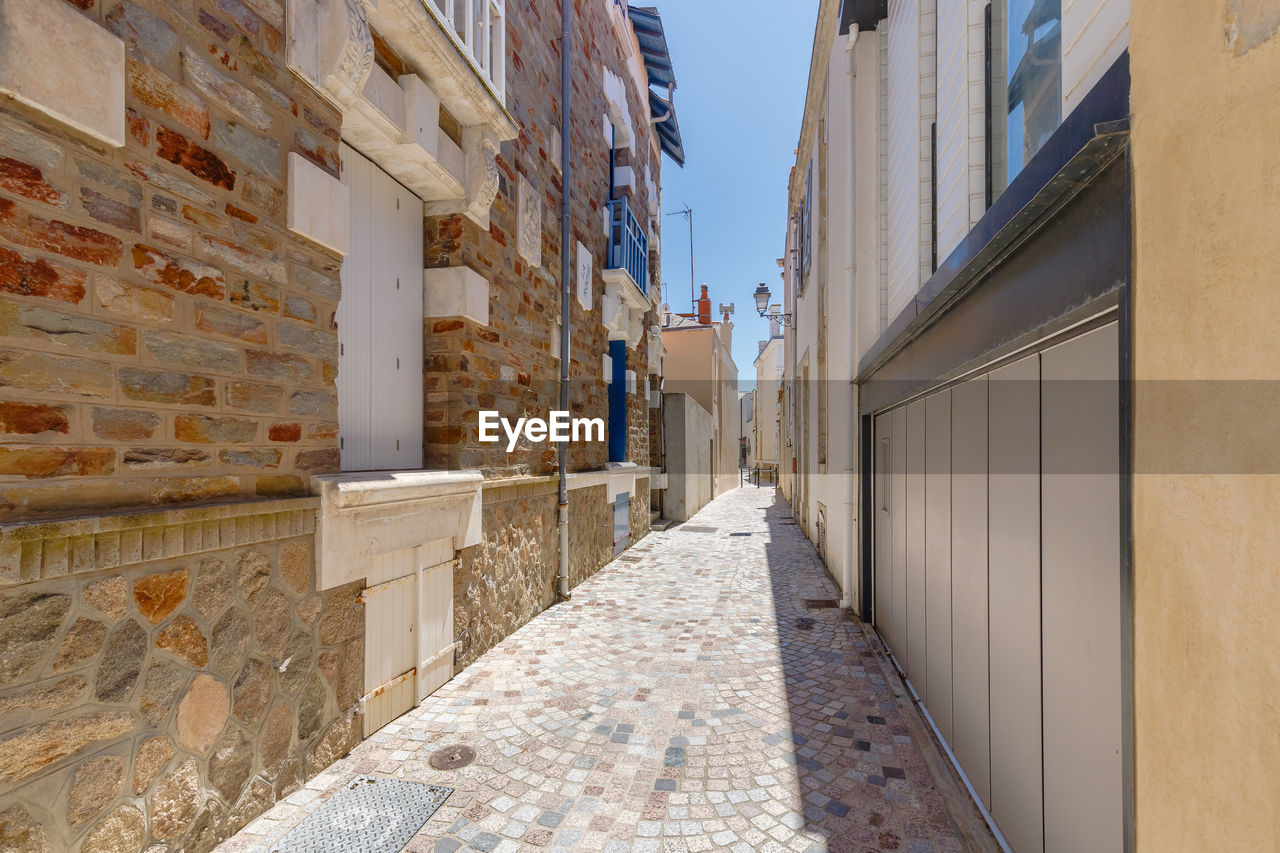 architecture, wall, building exterior, built structure, alley, building, city, facade, street, road, neighbourhood, town, residential district, day, footpath, nature, wood, urban area, outdoors, the way forward, house, sky, wall - building feature, no people, diminishing perspective, sunlight, narrow, travel destinations, travel