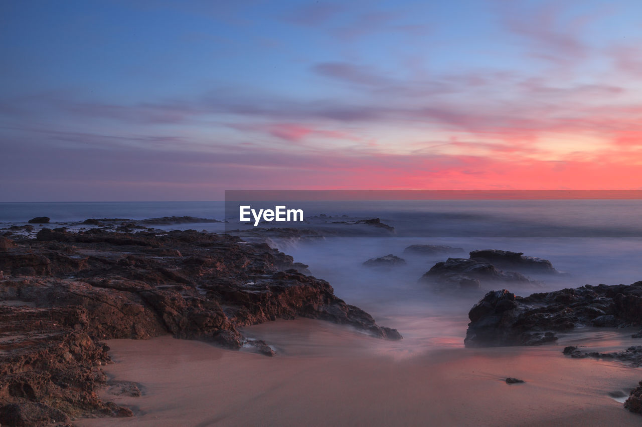 Rock formations in sea against cloudy sky during sunset