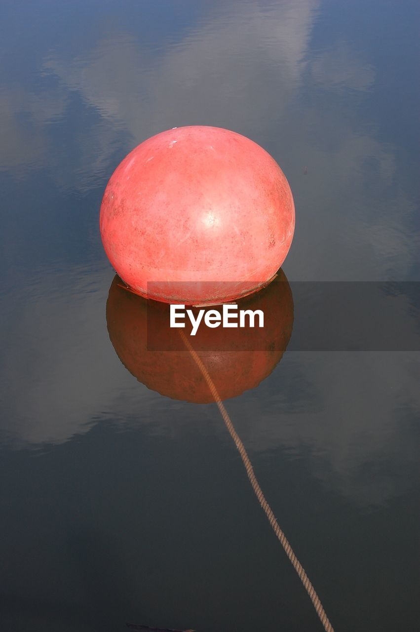 CLOSE-UP OF RED FLOATING ON WATER AGAINST LAKE