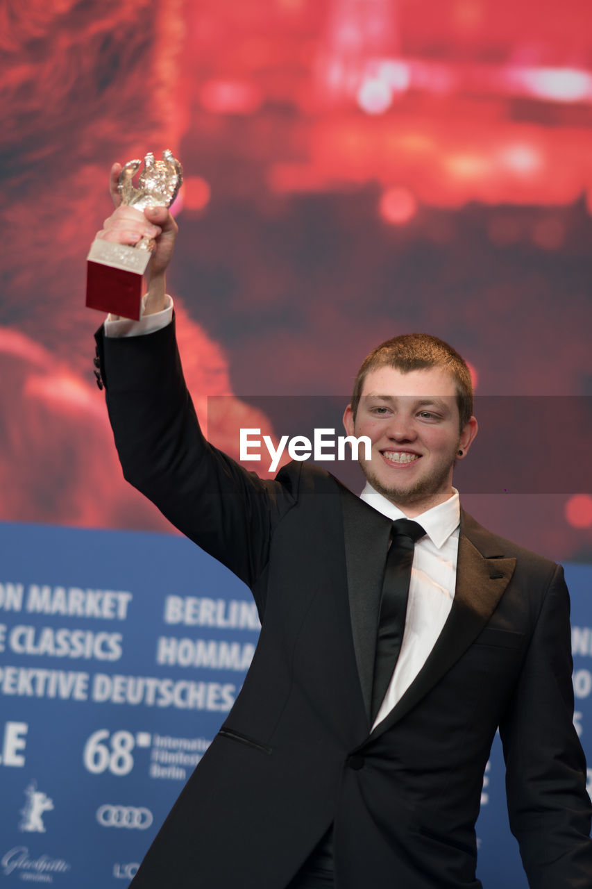 PORTRAIT OF SMILING YOUNG MAN STANDING AGAINST THE BACKGROUND