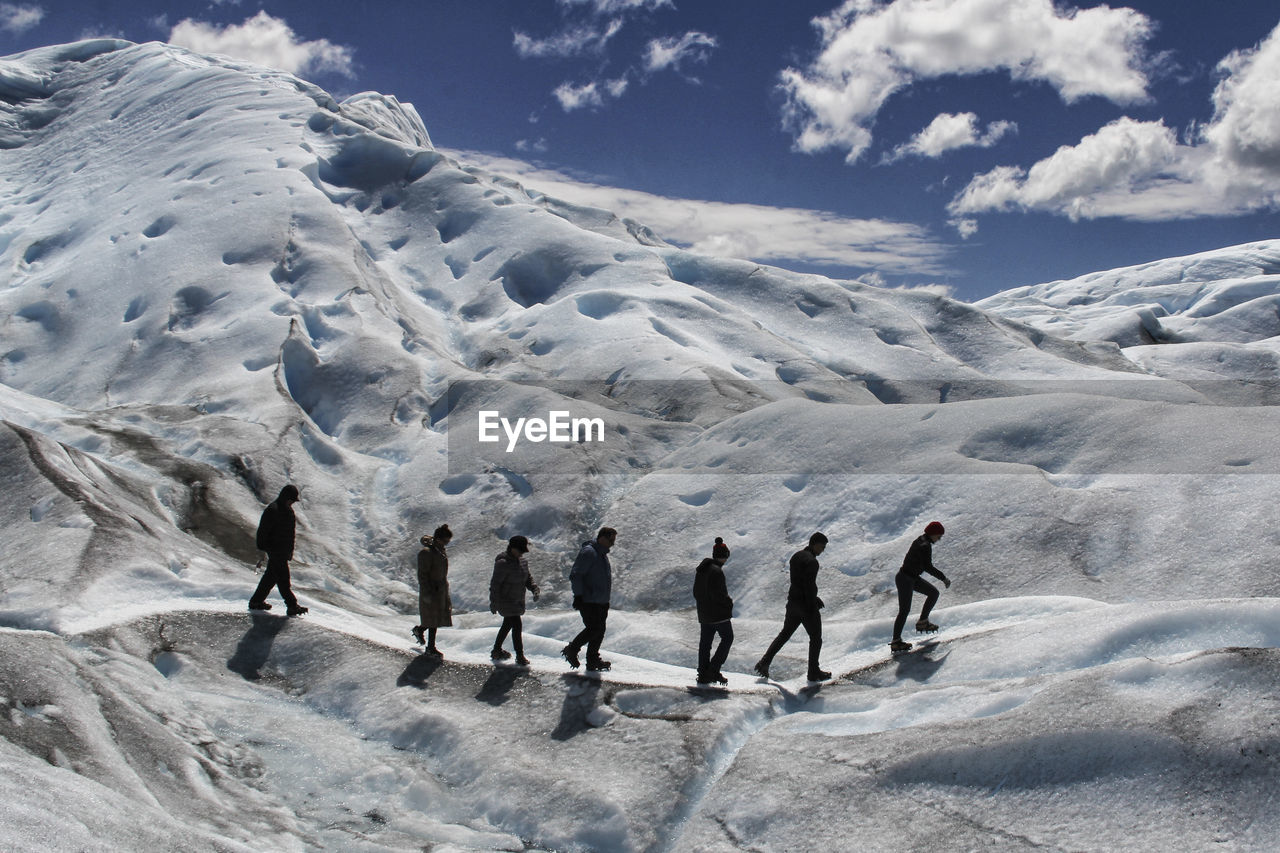 People walking on snowcapped mountain against sky