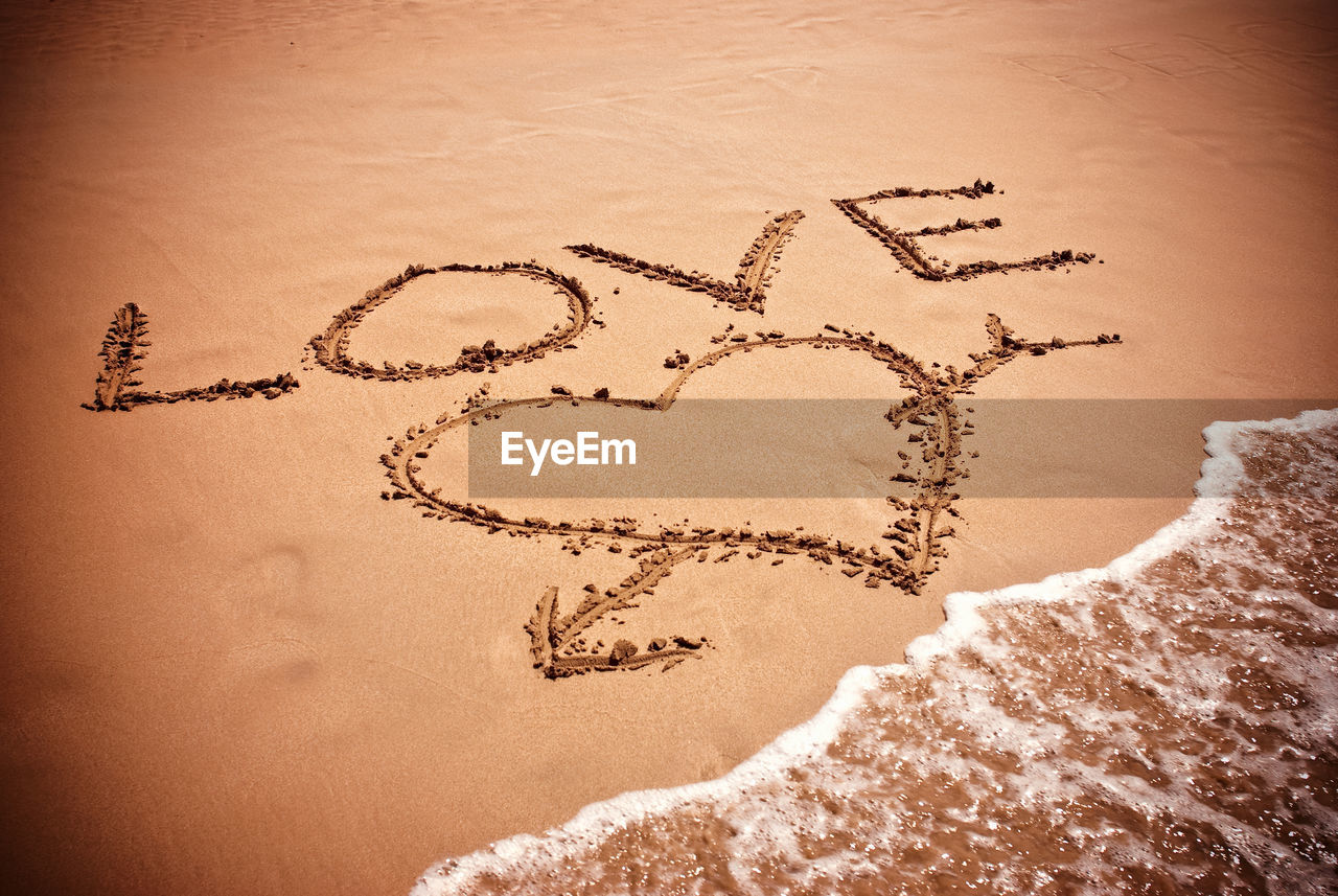 HIGH ANGLE VIEW OF TEXT ON HEART SHAPE ON SAND