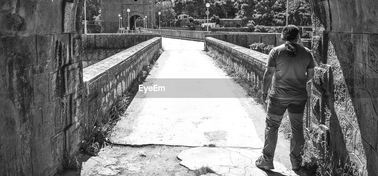 REAR VIEW OF MAN STANDING BY WALL