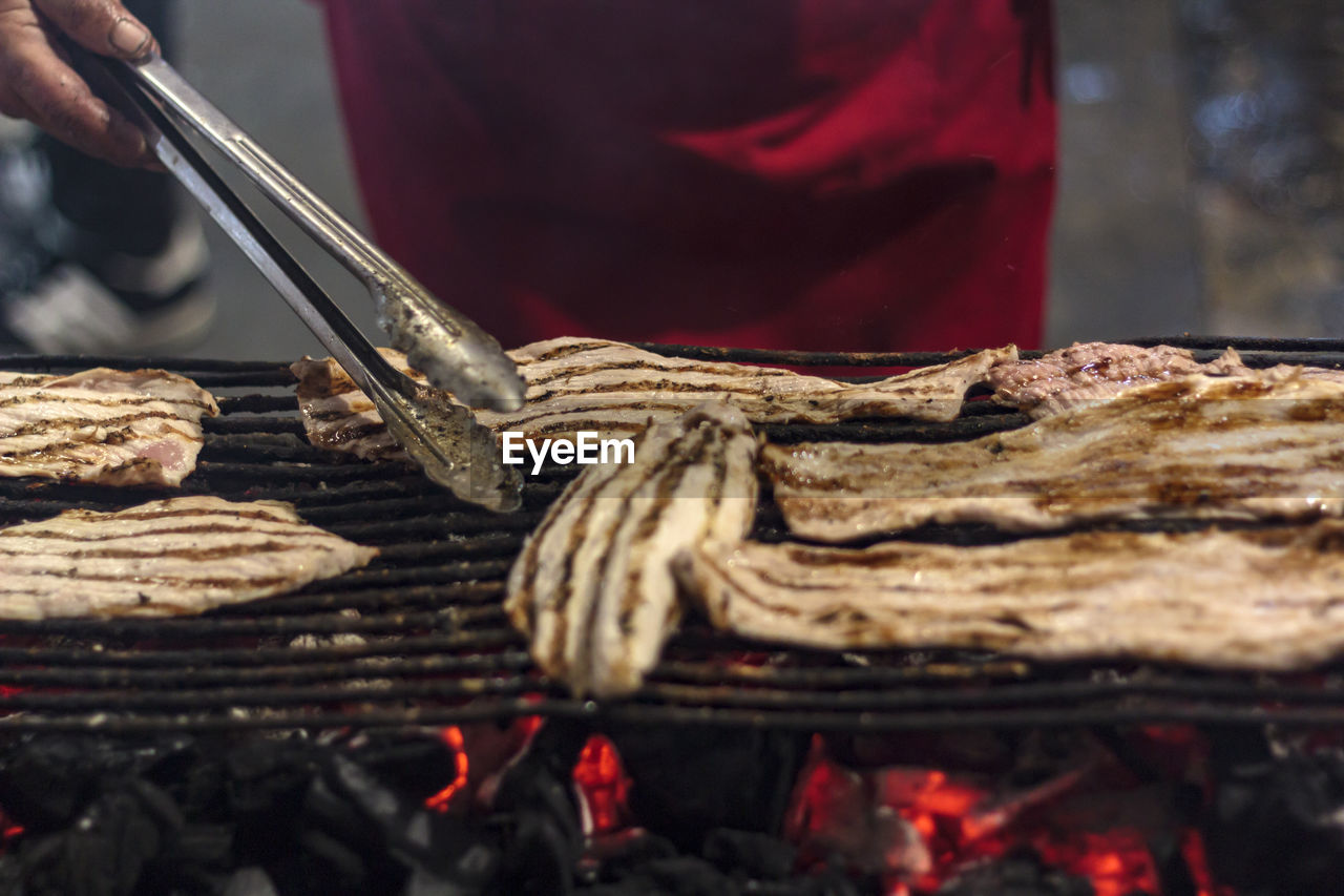 Woman grilling slices of pork steaks febras on the street during the feasts of the popular saints