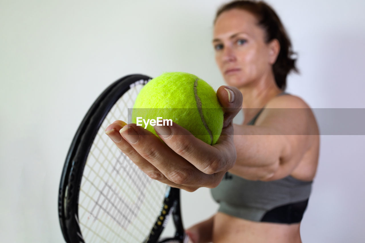 White woman prepares to serve in tennis. tennis ball and racket in the foreground.