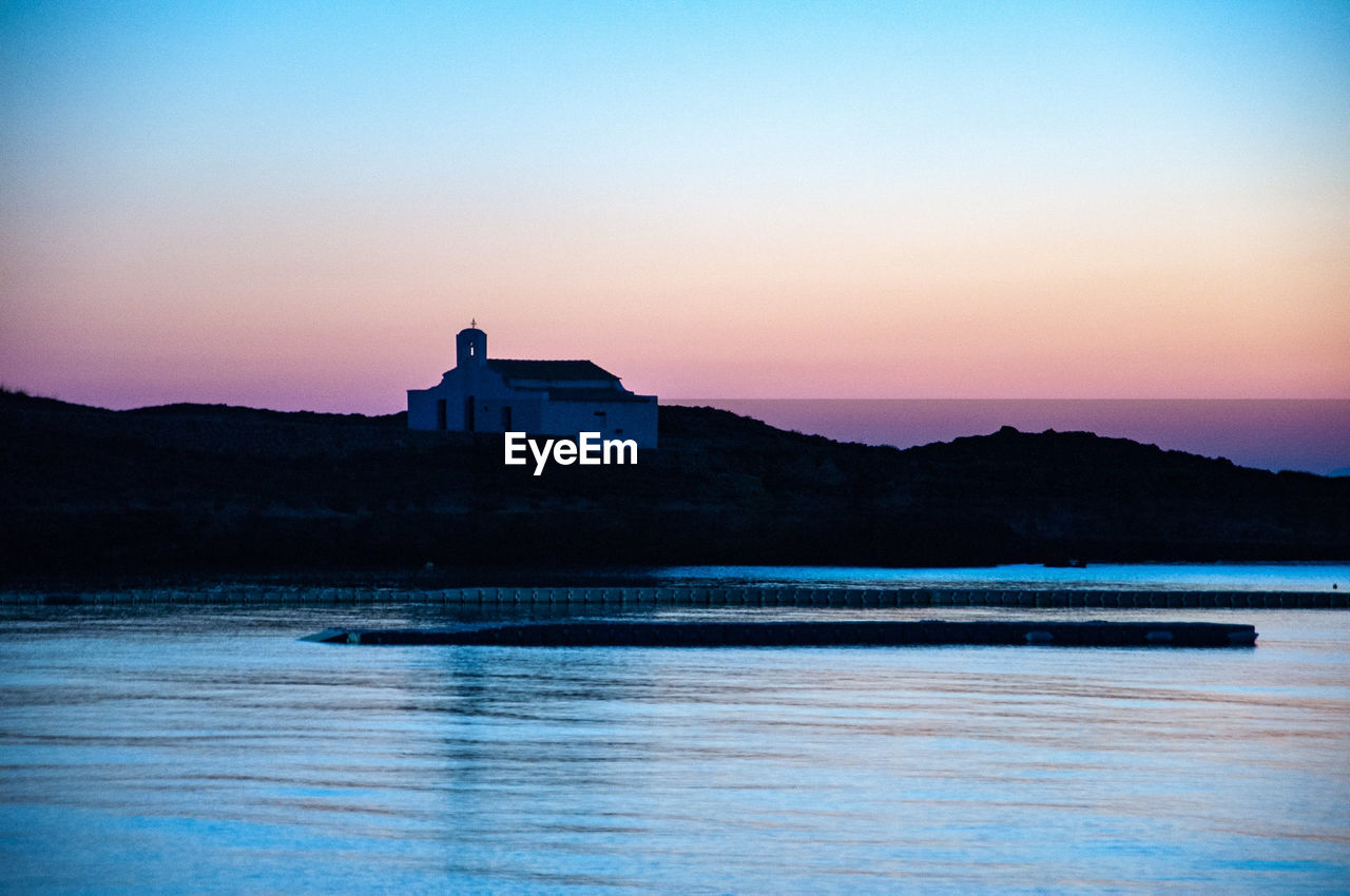 Building by sea against clear sky during sunset