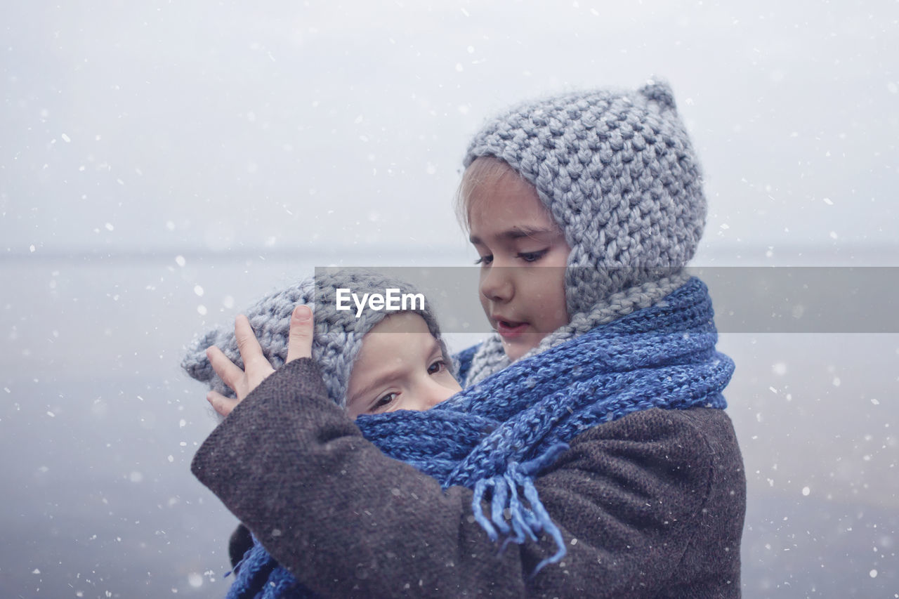 Cute of smiling siblings embracing by lake during winter